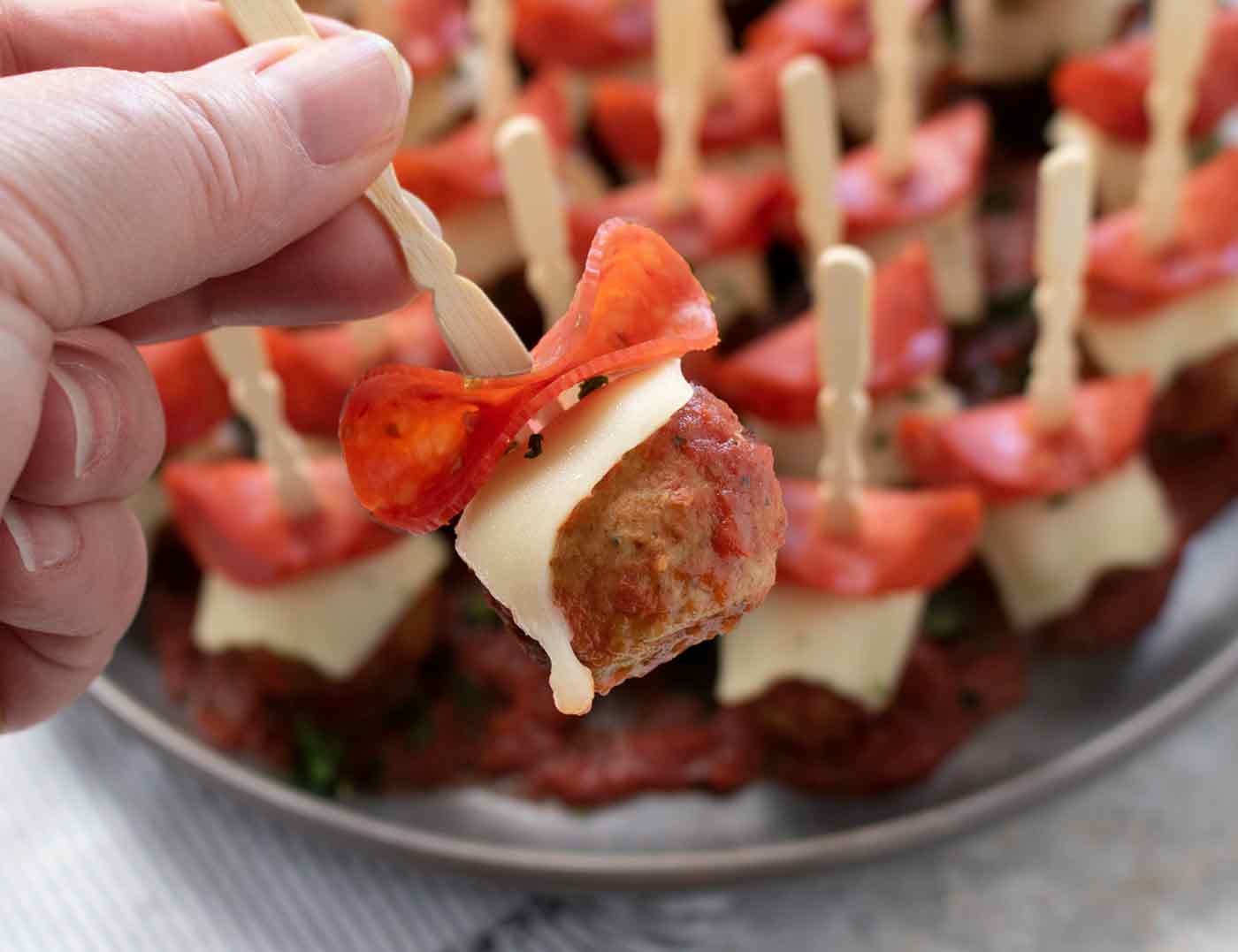Close-up of one assembled Pizza Meatball, with the plateful in the background.