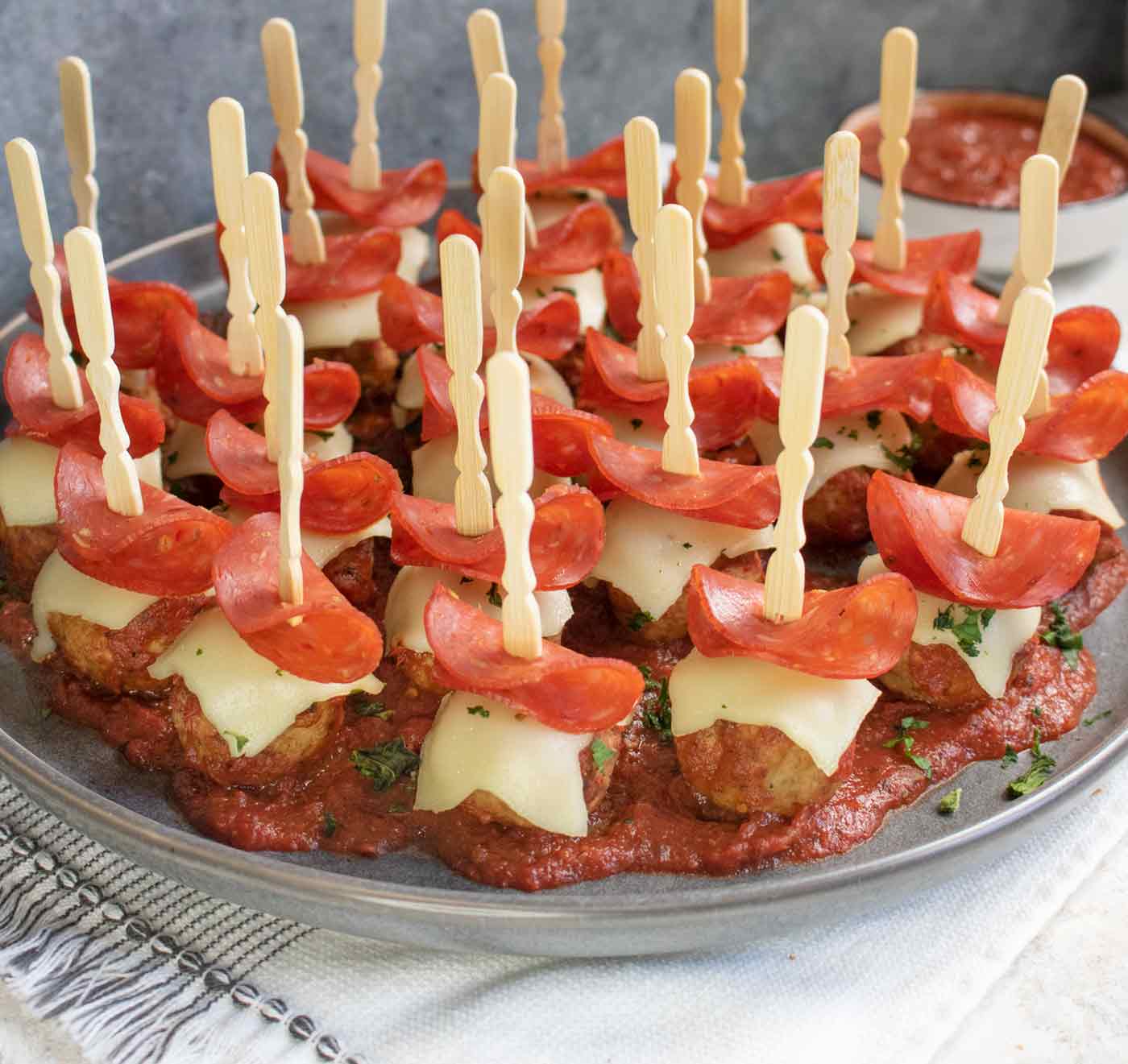 Easy Pizza Meatballs arranged on a dark gray plate, with a bowl of dipping sauce in the background.