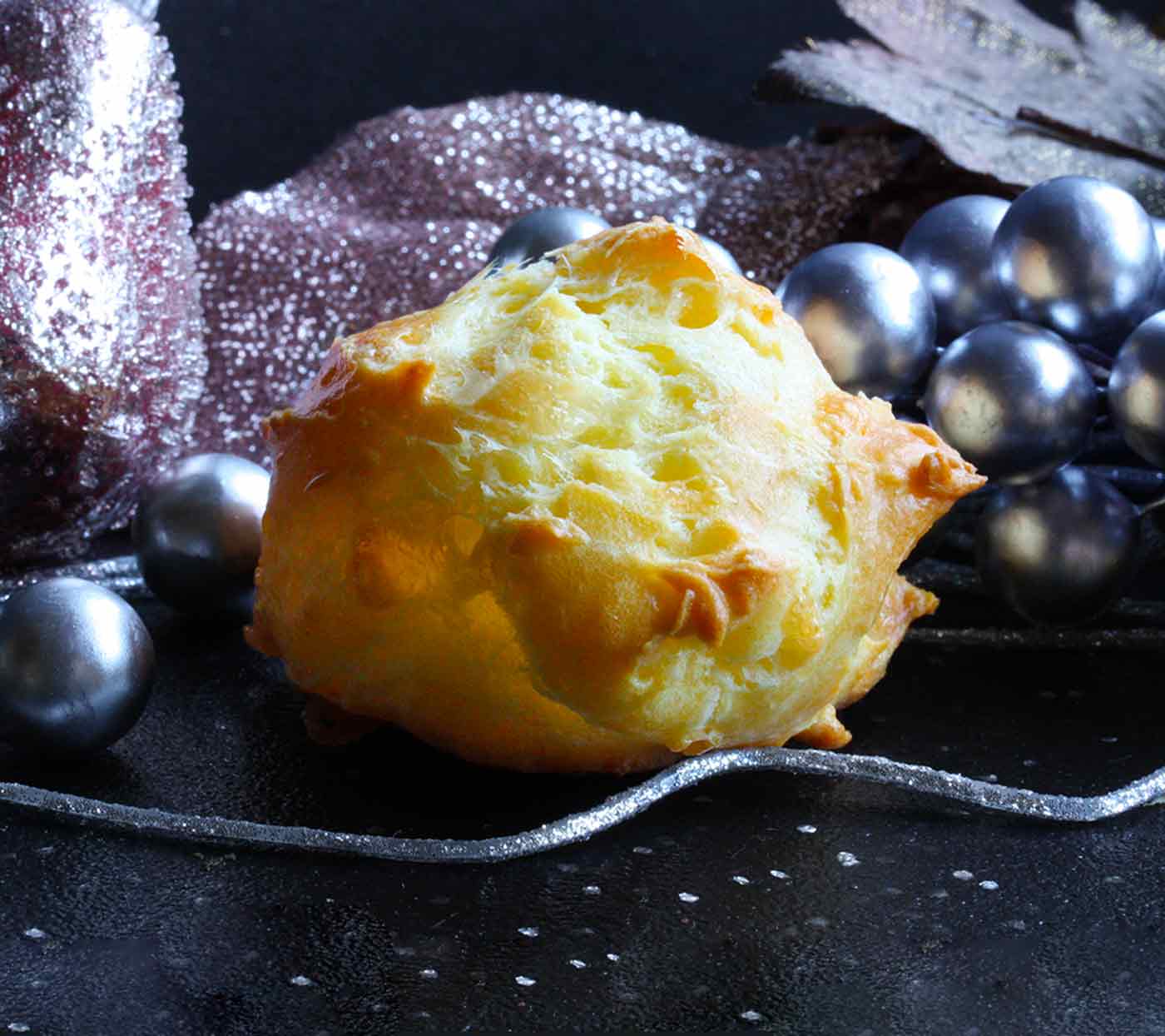 A puffy Gougere on a dark board with Christmas decorations.