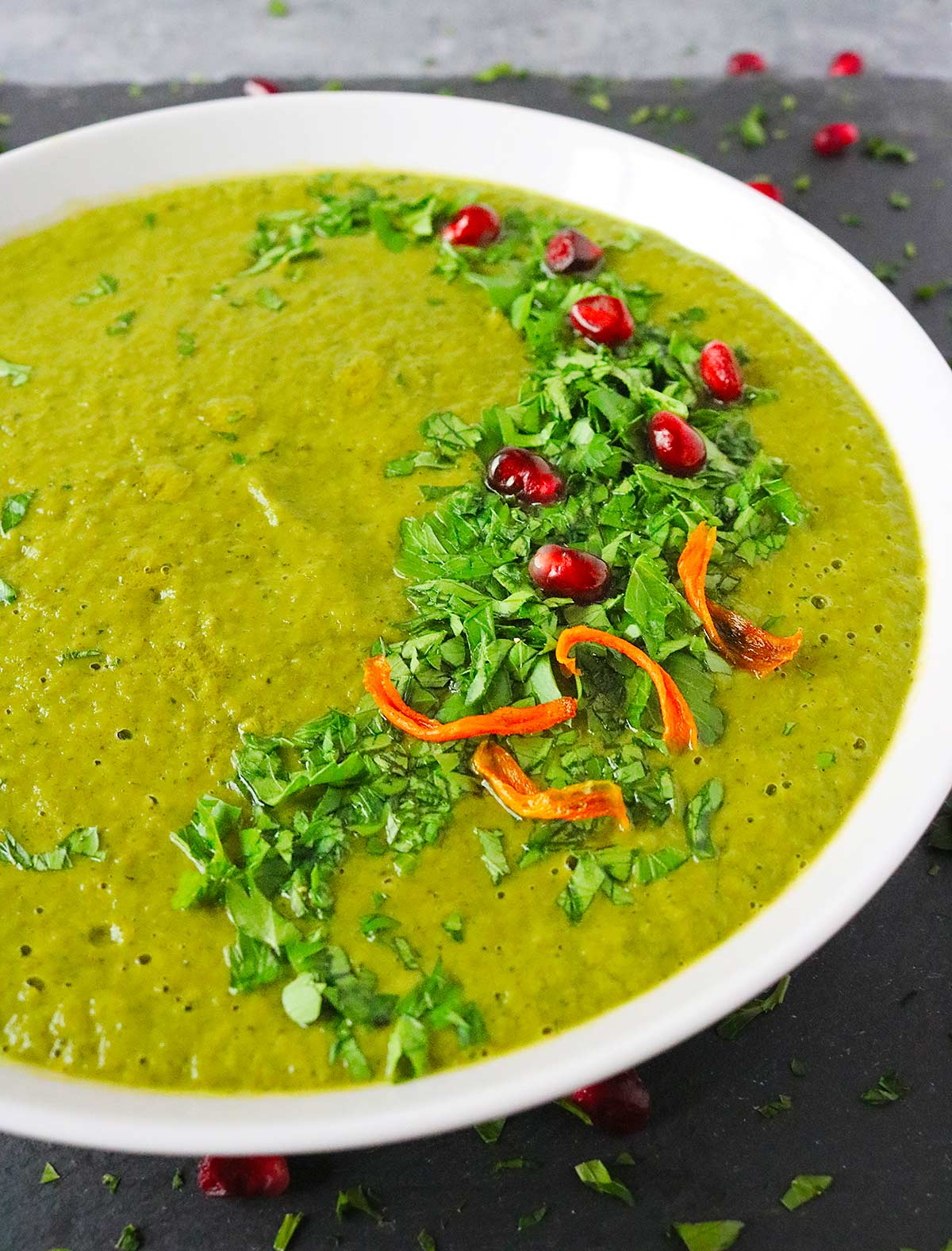 Angled view of Green Soup in a white bowl with garnishes.
