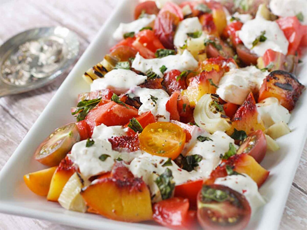 Side angled view of Grilled Peach Fennel Tomato Salad on a white rectangular platter.