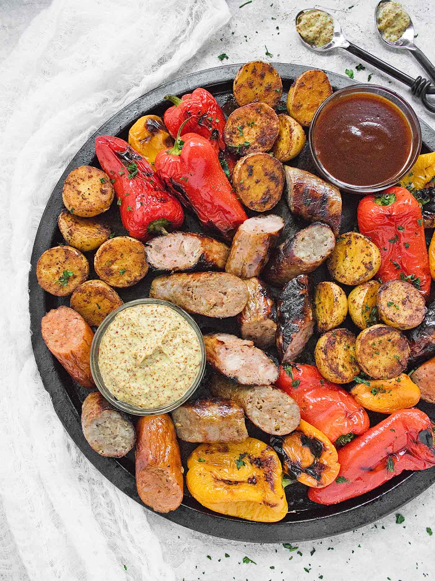 Overhead shot of platter of grilled sausages, peppers, potatoes with dipping sauces