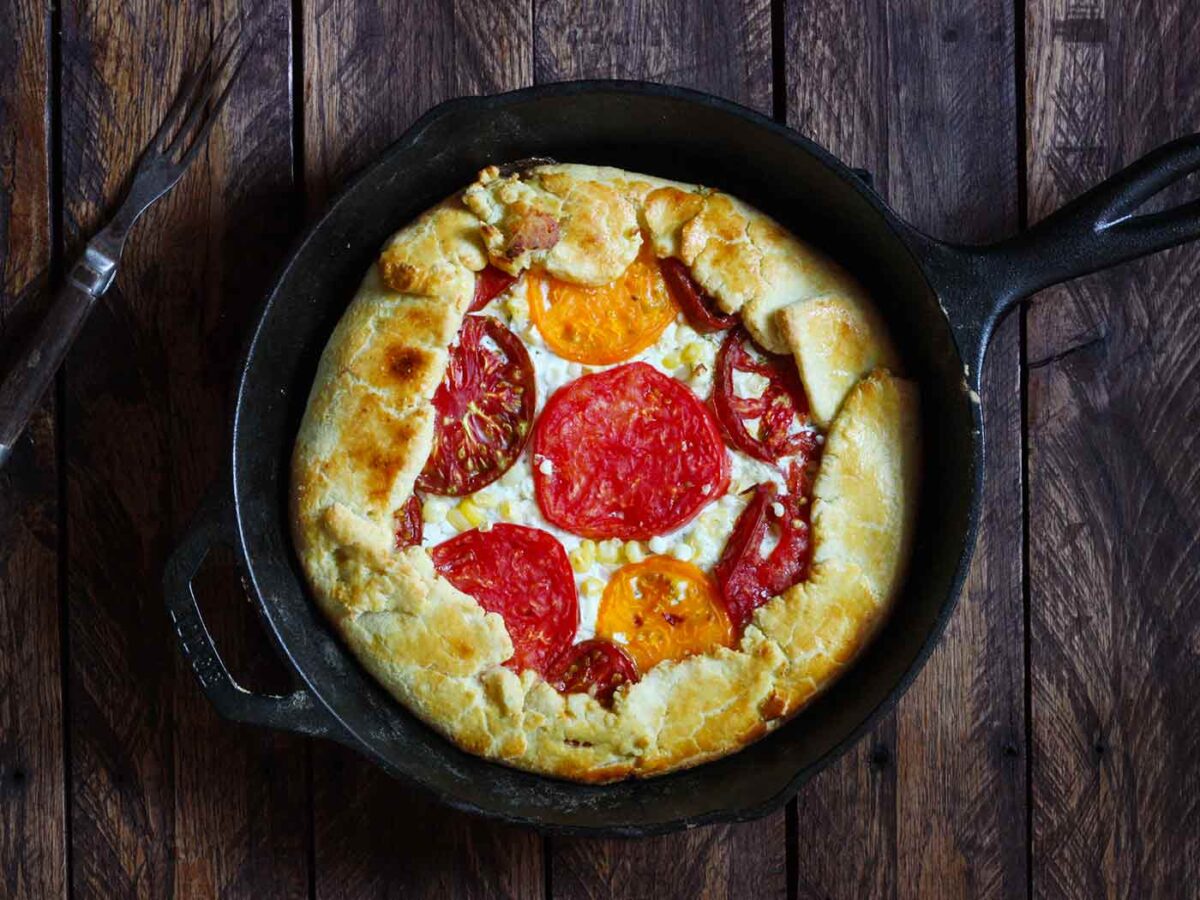 Overhead view of Grilled tomato corn galette in a cast iron pan on a wooden surface.