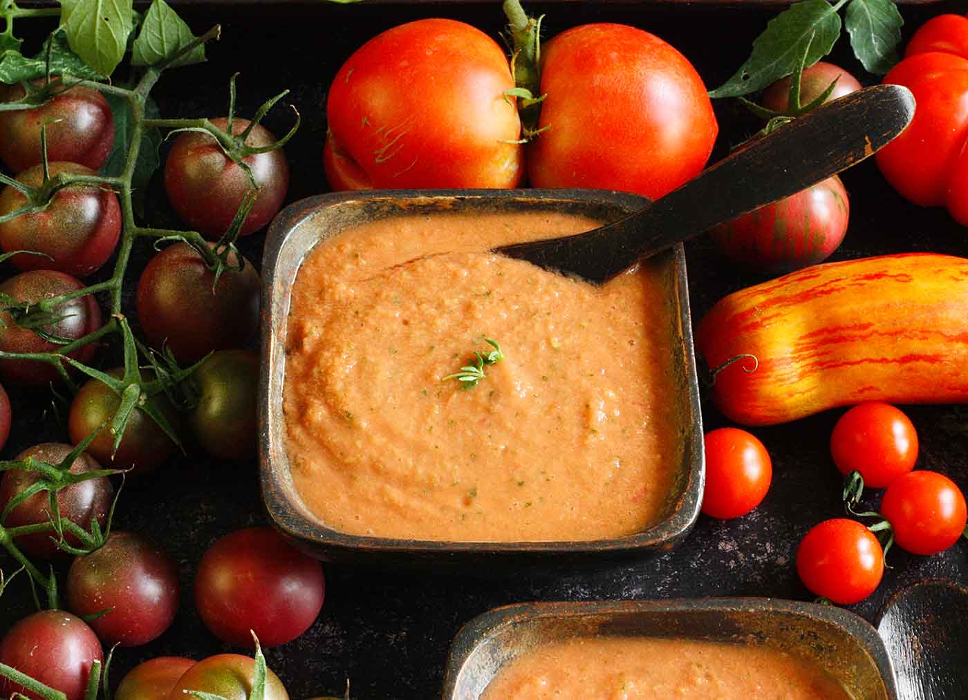 Guaczpacho in a square bowl surrounded by tomatoes