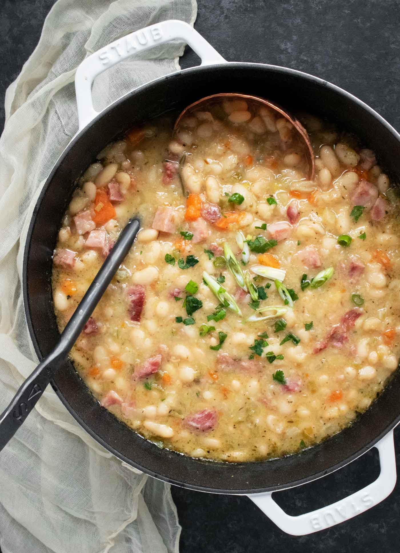 An overhead view of a pot of Ham and Bean Soup, with a copper, cast iron soup ladle.