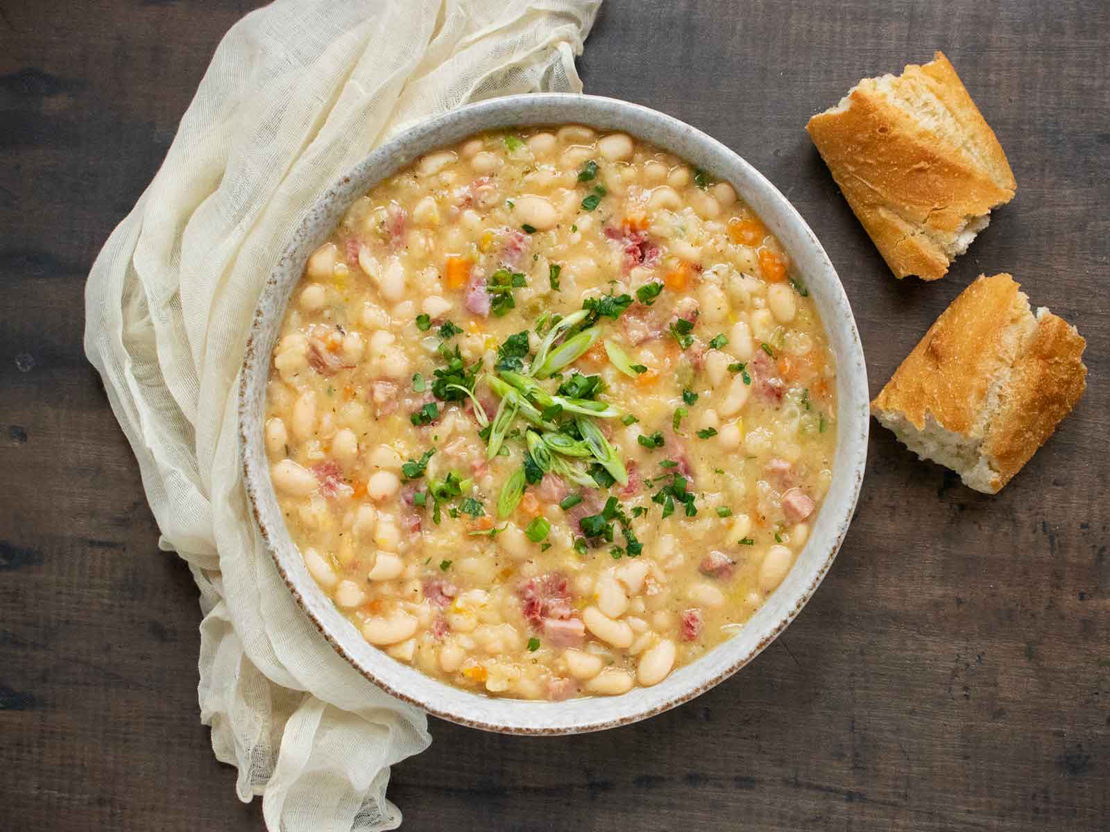 Ham and Bean Soup in a white bowl with a side of bread.