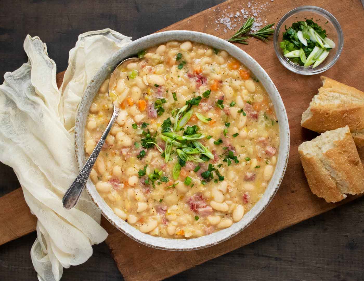 Overhead view of Ham and Bean Soup in a bowl with a spoon and a side of bread.