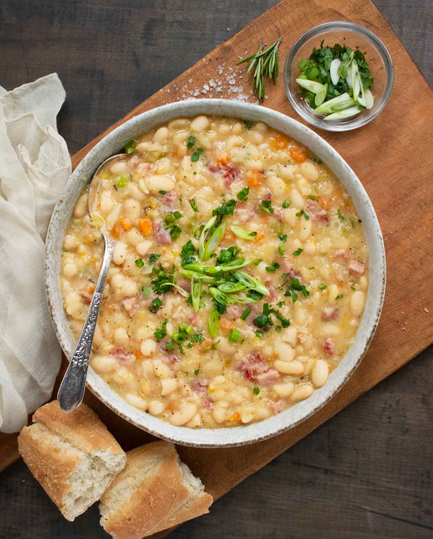 An overhead photo of Ham and Bean Soup in a gray bowl with a spoon, and a side of bread.