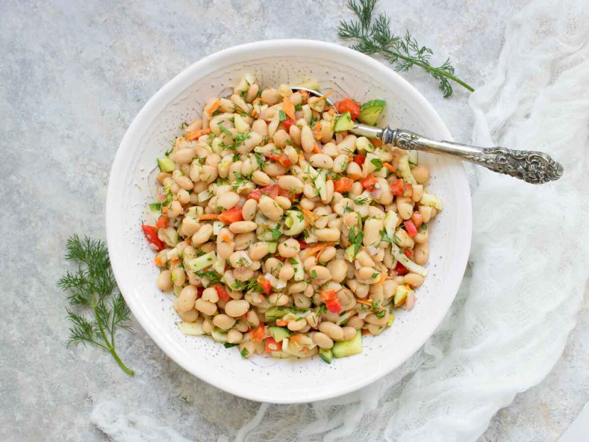 Overhead view of Herbed White Bean Picnic Salad in a white serving bowl with a spoon.