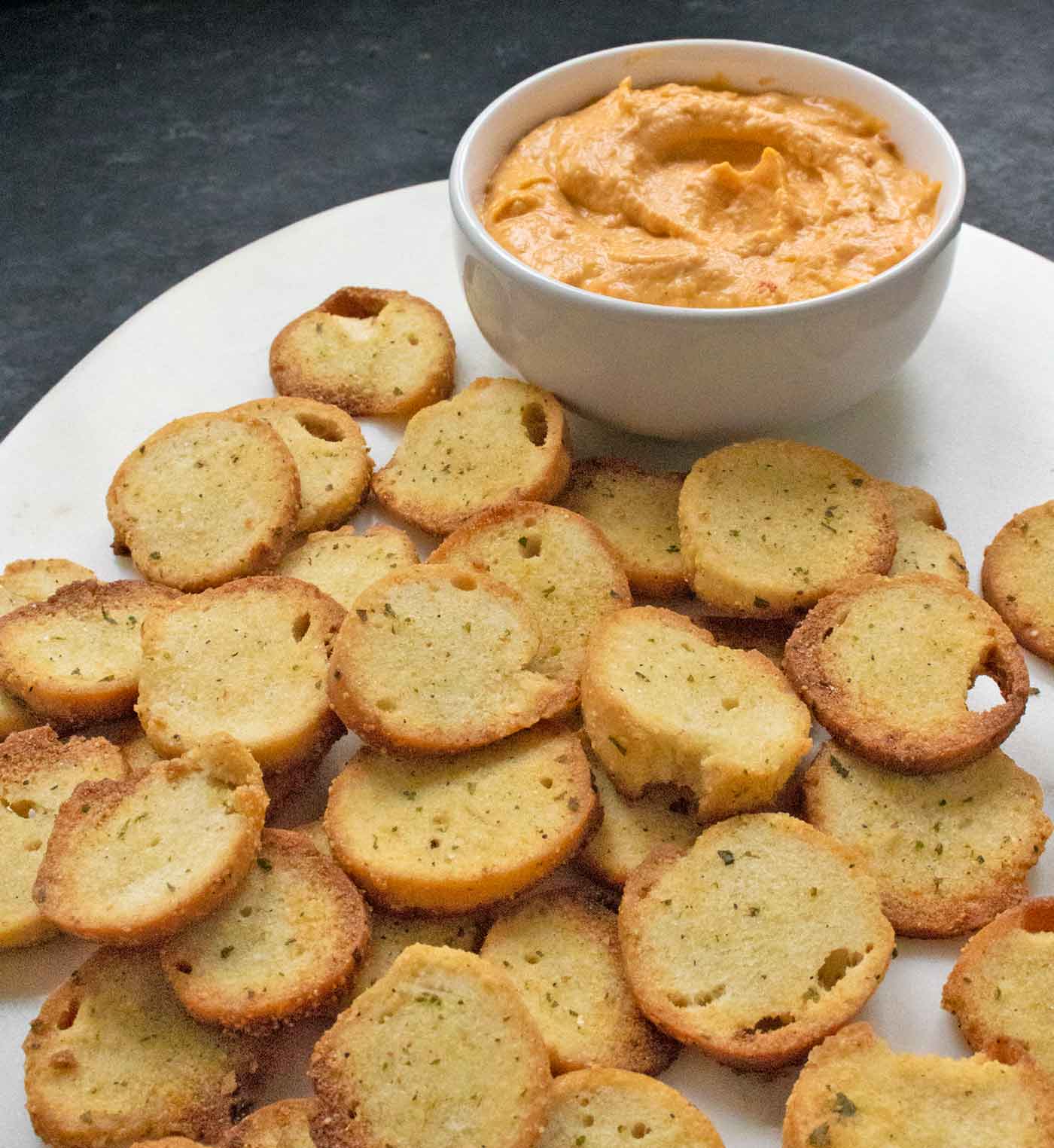 Ranch flavored Homemade Bagel Chips on a marble serving board with a side of roasted red pepper hummus.