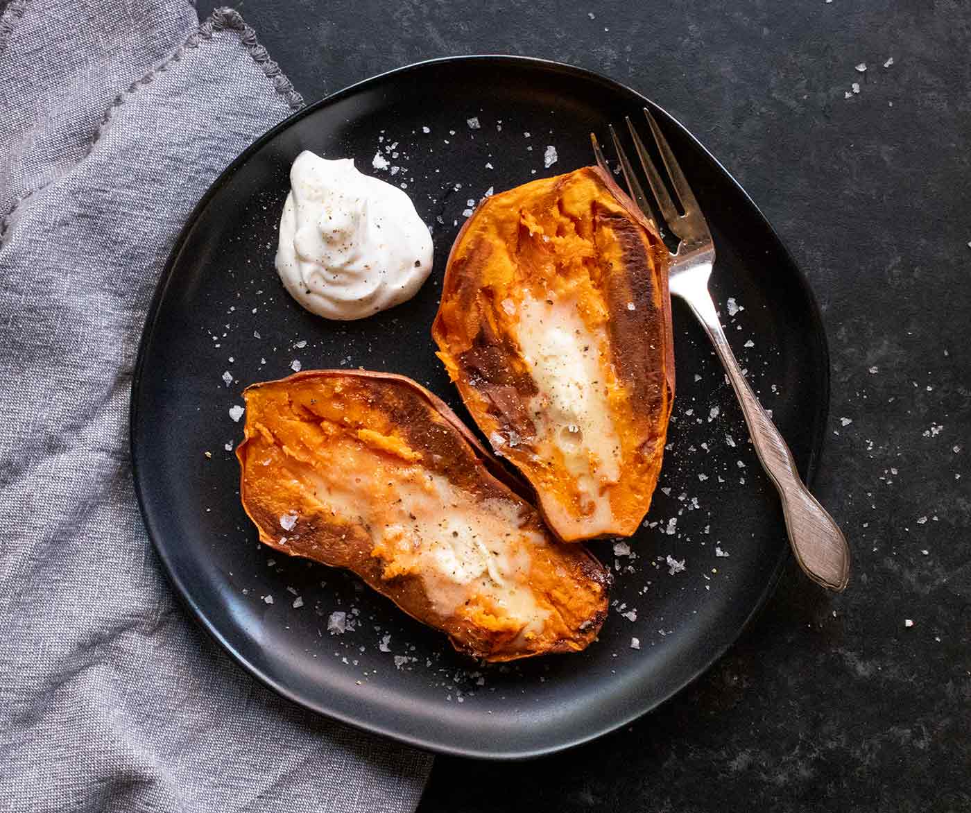 Two sweet potato halves, freshly baked, on a black plate.