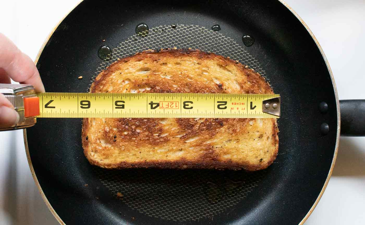 Fried toast in a skillet with a hand holding a tape measure over the bread to show the width of the bread, which is 6 inches.