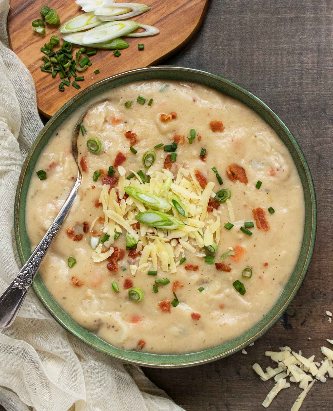 View from above of Irish Potato Soup in a green bowl, with a spoon, and toppings on the side.