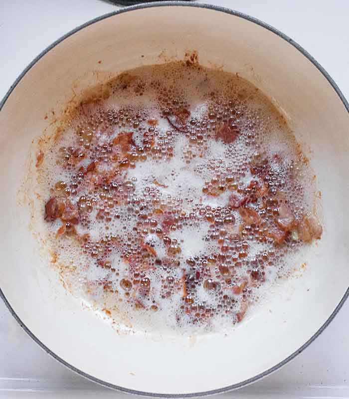 Bacon crisping up and browning in the pot, with the rendered fat gently foaming in spots.