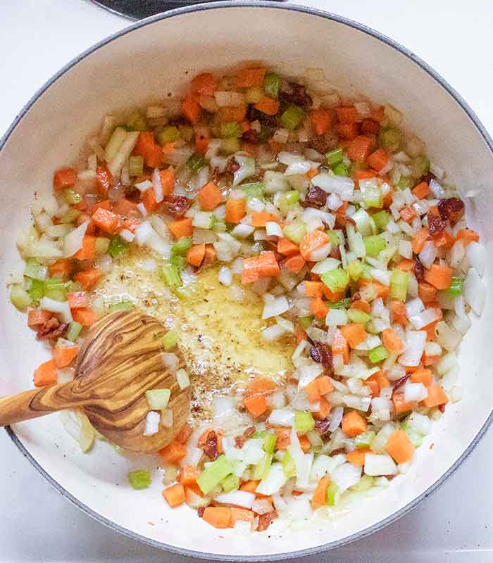 Using a wooden spoon to scrape up the fond left behind by the bacon.