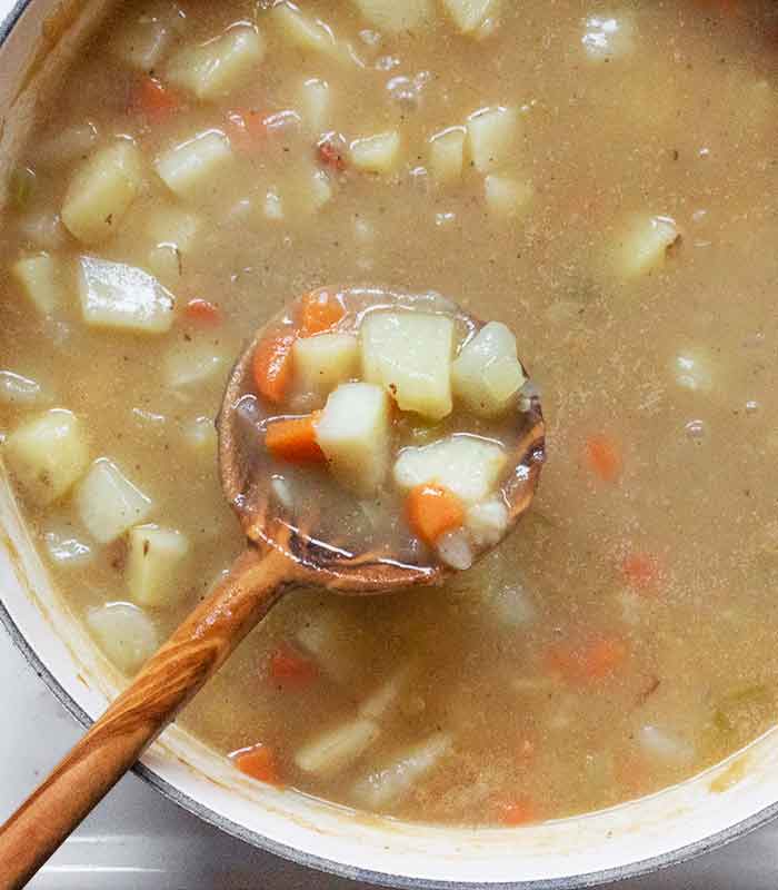A large wooden spoon scooping out potato pieces to move to a bowl, to re-add later.