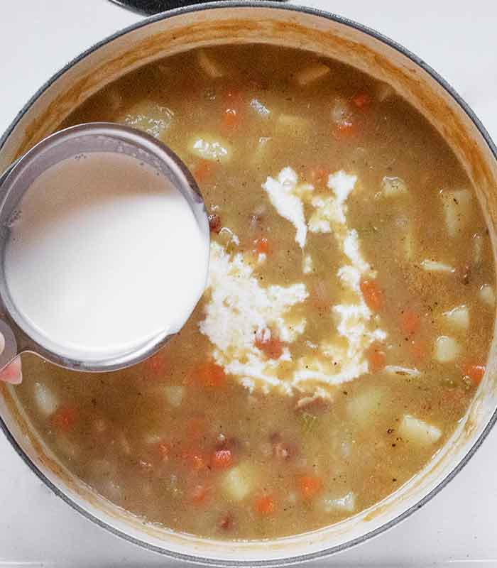 Pouring heavy cream into the soup from a measuring cup.