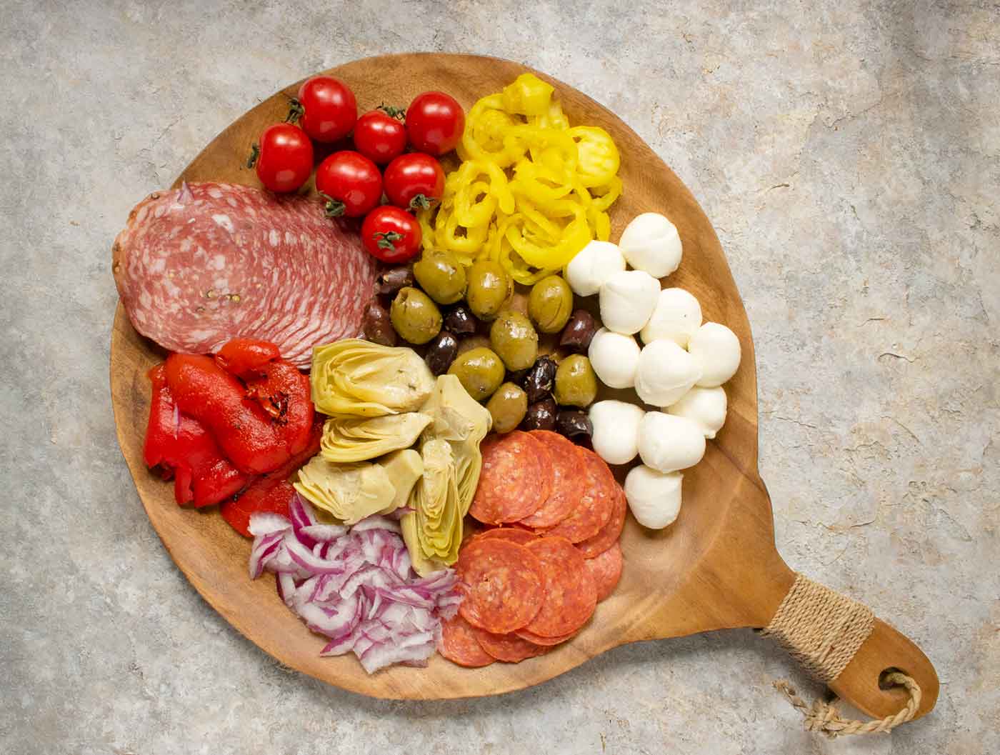 The main ingredients of Italian Antipasto Salad arranged on a round wooden board.