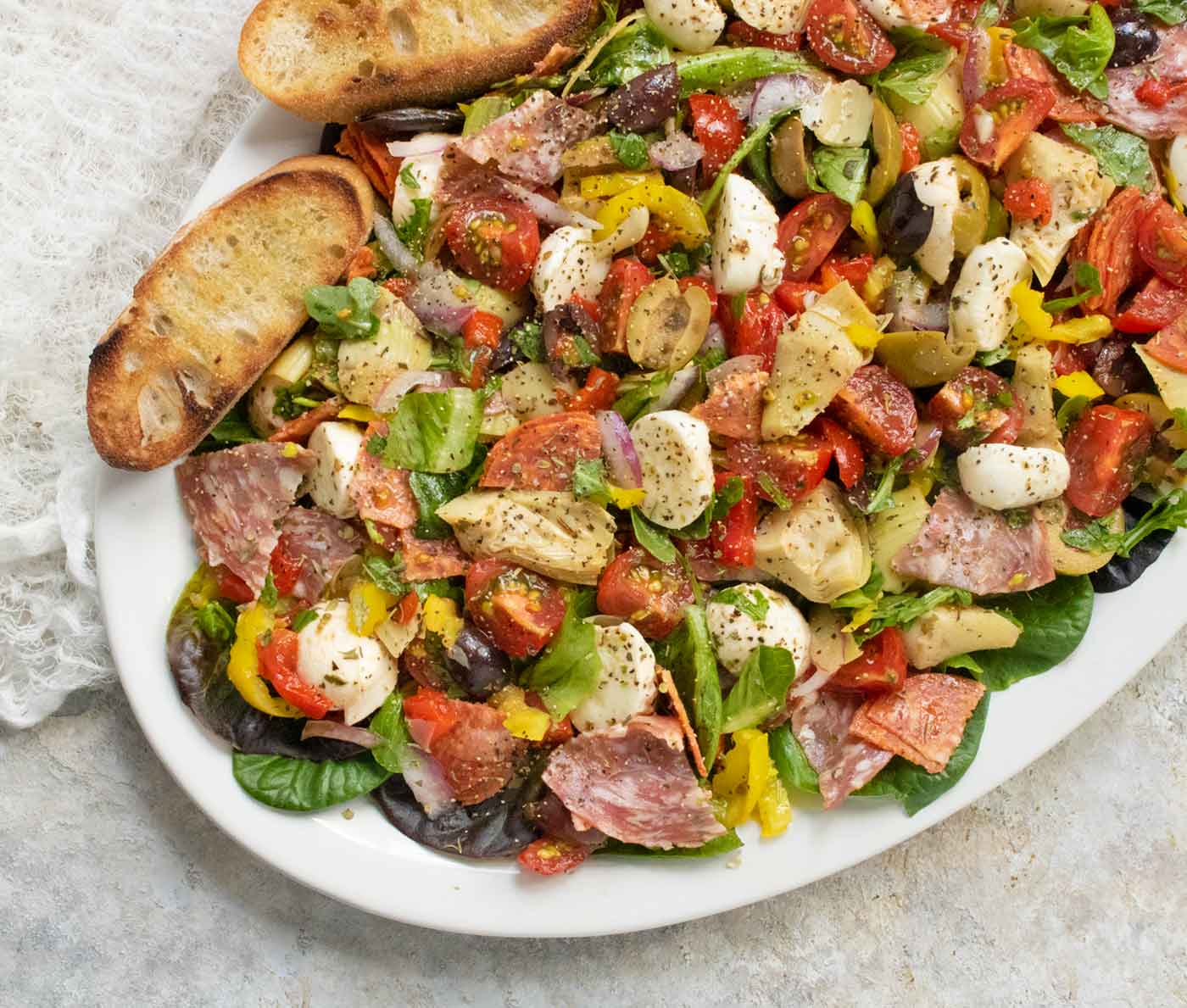 An overhead, angled view of a platter of Italian Antipasto Salad with toasted bread on the side.