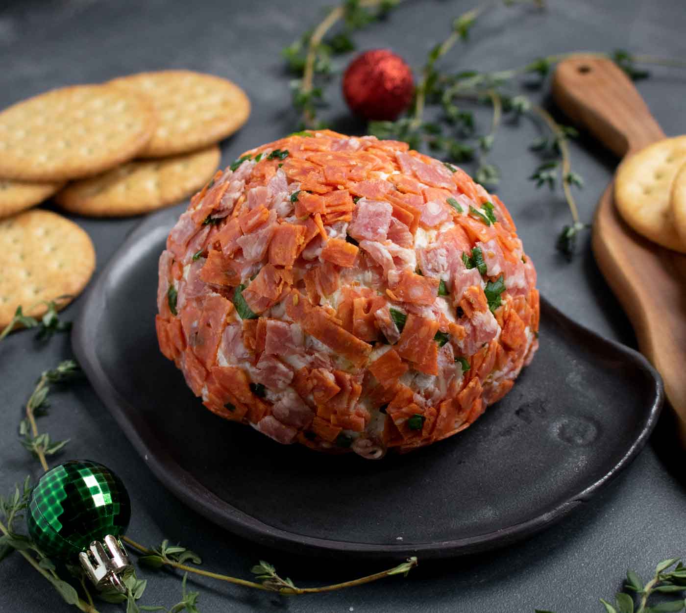 Italian Grinder Cheese Ball on a black serving plate with crackers.