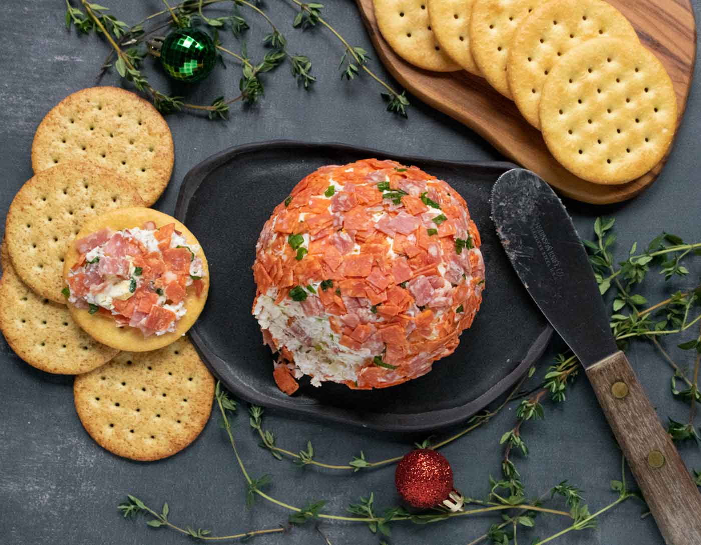 Overhead view of an Italian Grinder Cheese Ball on a black serving plate with crackers.