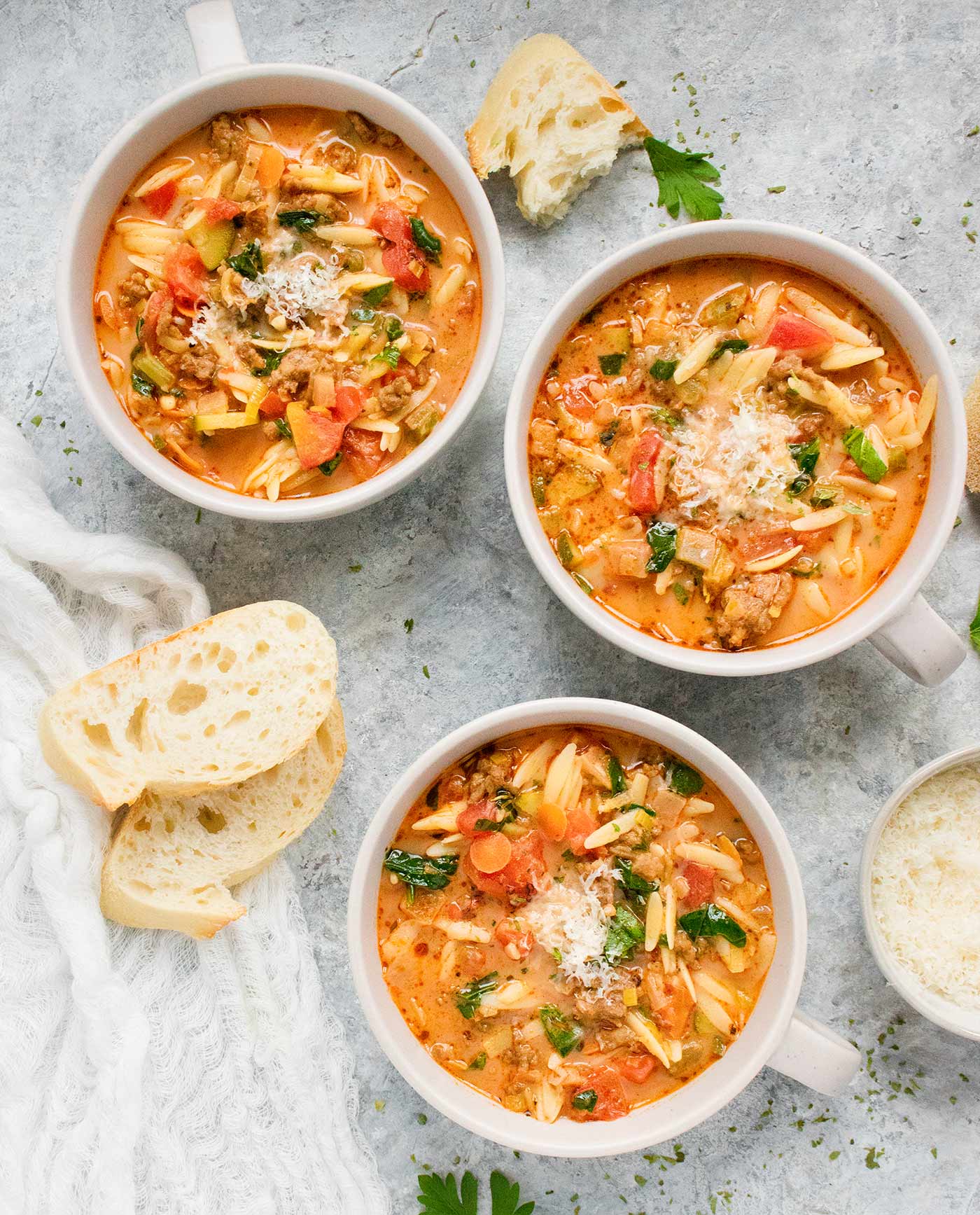 Three bowls of Italian Sausage Orzo Soup with a side of sliced French baguette