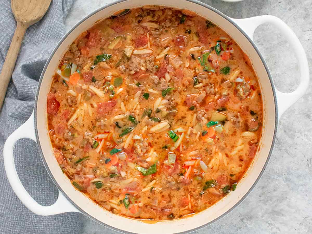 Overhead view of Italian Sausage Orzo Soup in a white Dutch oven.