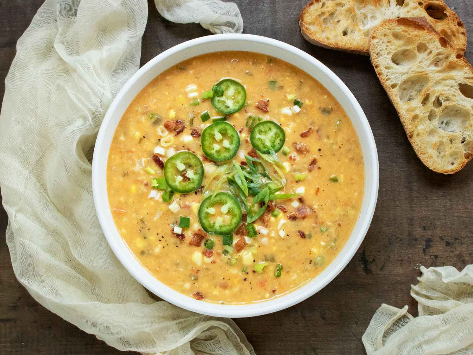 Overhead view of a bowl of Jalapeno Bacon Corn Chowder with slices of toasted bread on the side and napkins.