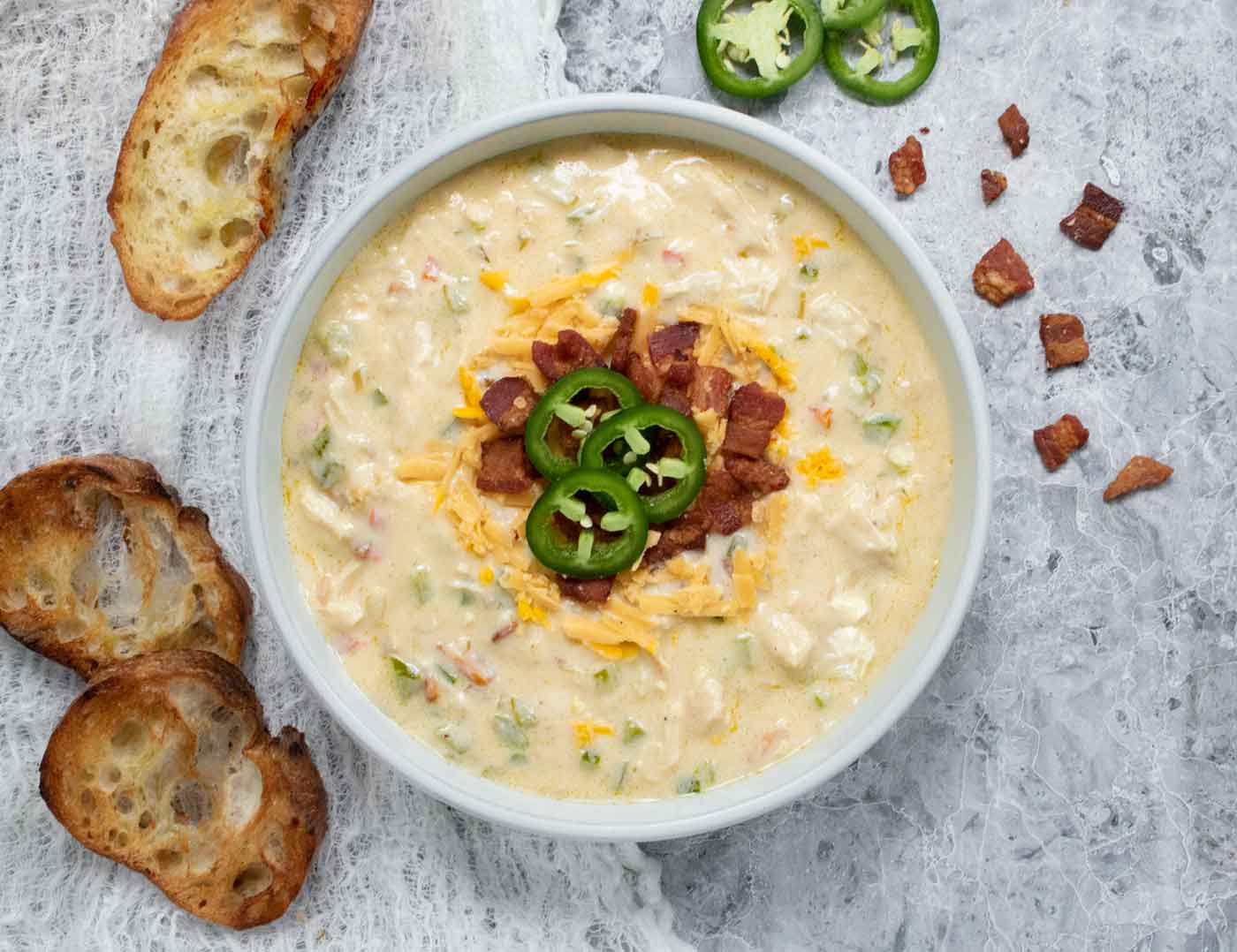 Overhead view of a bowl of Jalapeno Popper Chicken Soup with sliced bread on the side.
