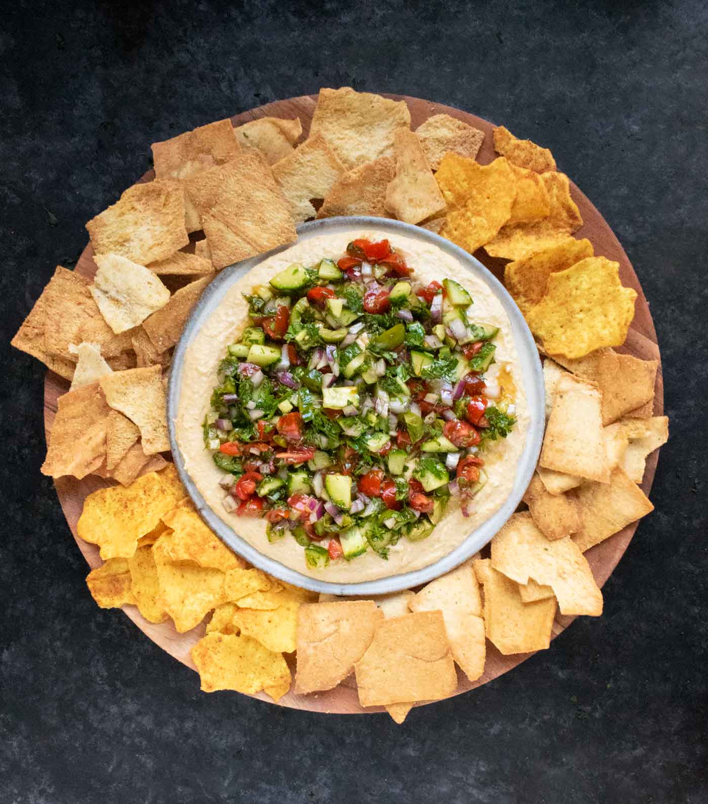 Layered Veggies & Hummus Dip on a serving platter with chips arranged around the edges.