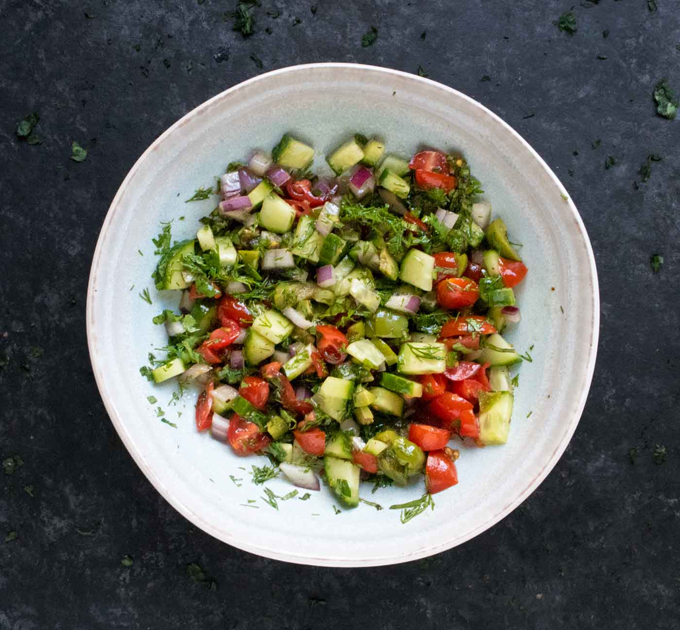 A bowl of marinated chopped vegetables and herbs.
