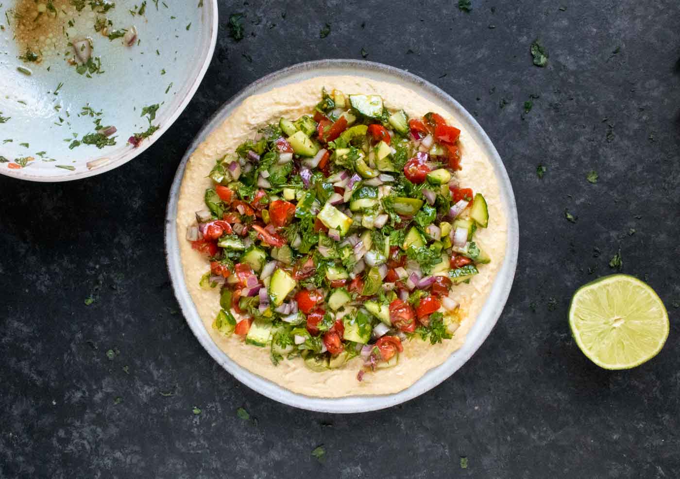 Marinated vegetables layered over hummus on a plate.