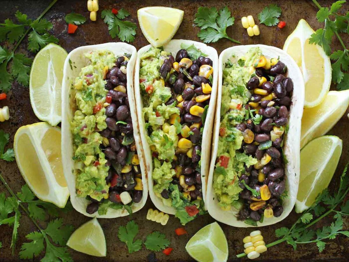 Three vegetarian guacamole tacos lined up on a baking sheet.