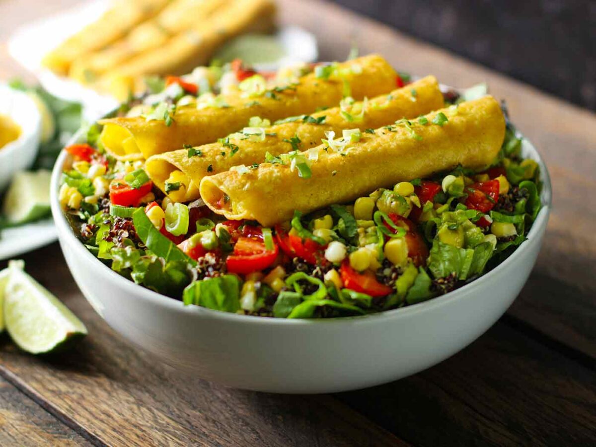 Side view of a mango avocado salad topped with taquitos.
