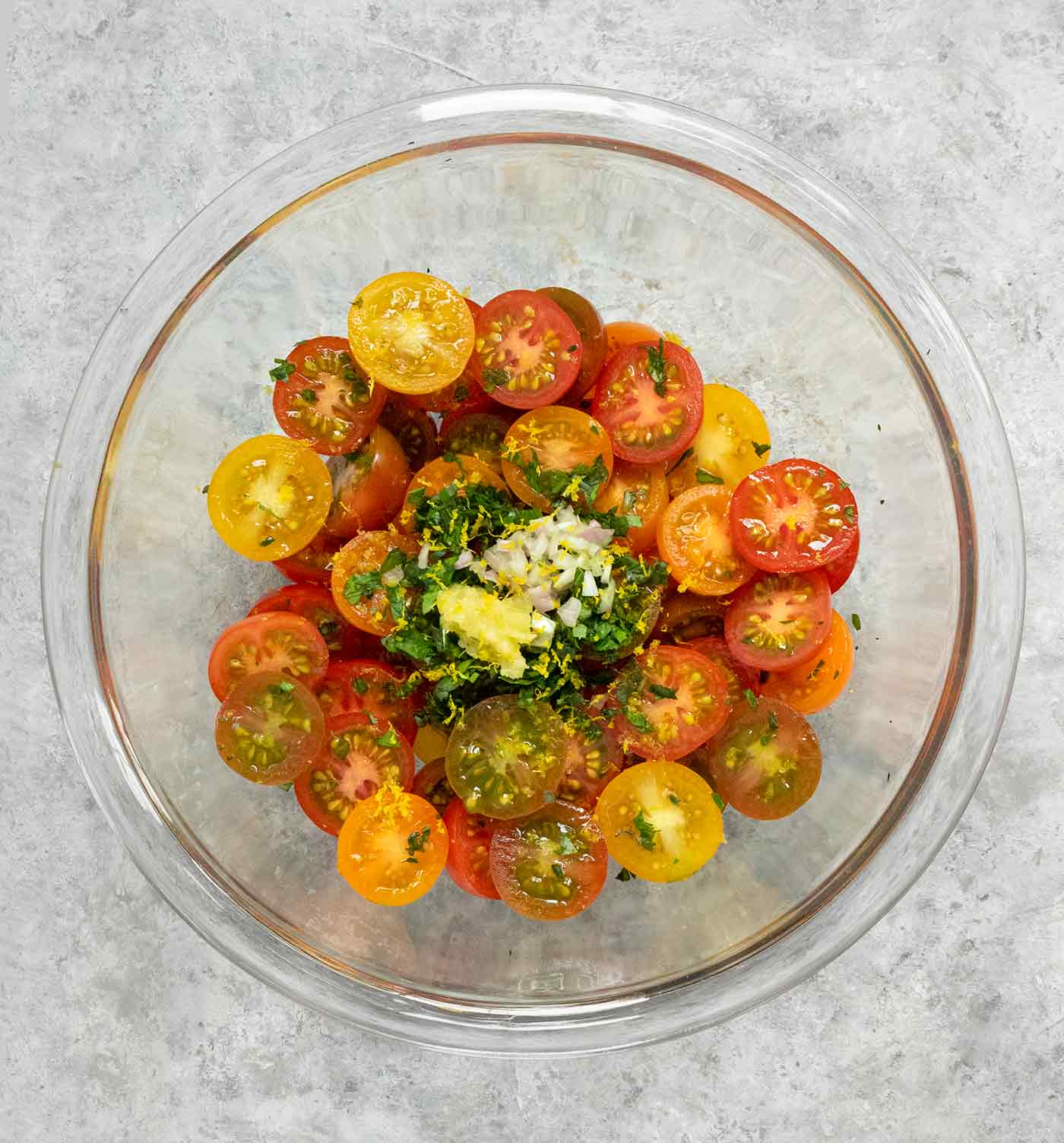 A bowl of sliced cherry tomatoes with fresh herbs, minced garlic, and chopped shallots.
