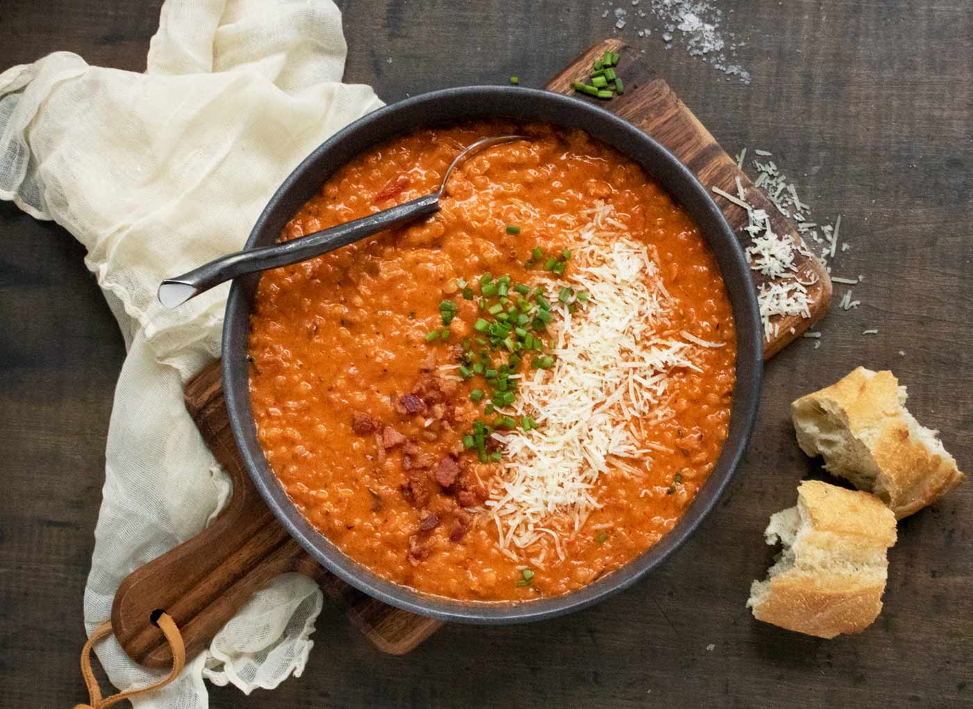 Overhead view of a bowl of Marry Me Red Lentil Soup with a spoon and bread slices on the side.