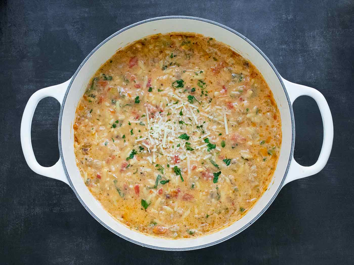 Overhead view of Marry Me Sausage Orzo Soup in a large white Dutch oven on a black background.