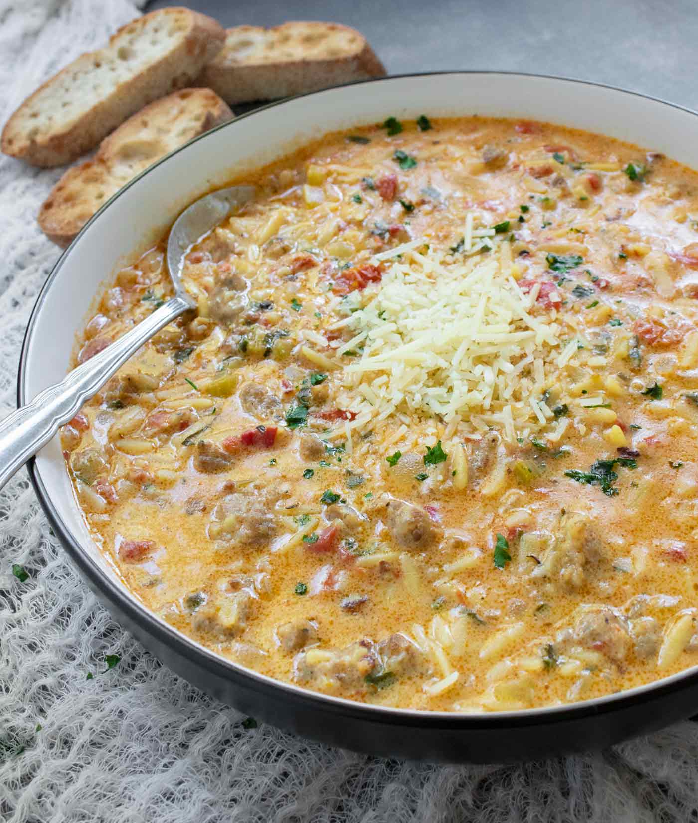 Side angled view of Marry Me Sausage Orzo Soup in a white bowl with a black rim, and a side of bread.