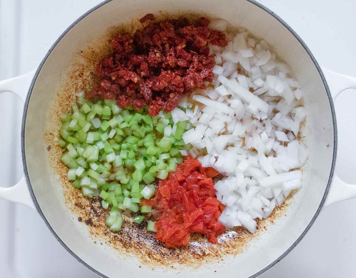 Onions, celery, roasted red peppers, and sun dried tomatoes cooking in a white Dutch oven.