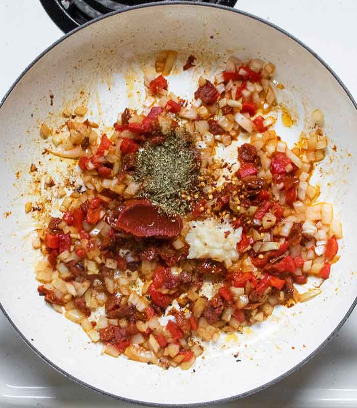 Adding the tomato paste and seasonings to the vegetables.