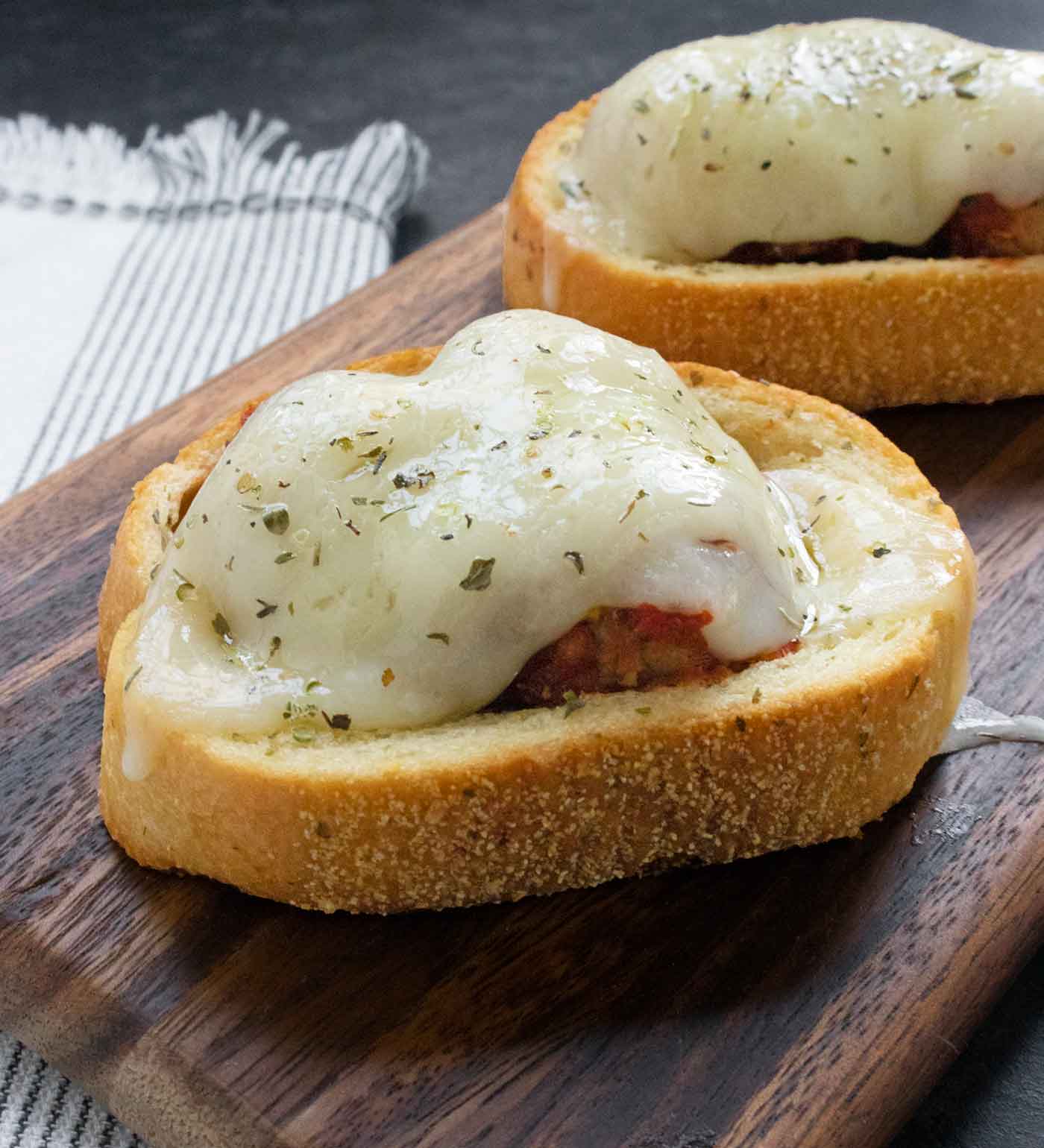 Side-angled view of a pair of Meatballs on Texas Toast on a wooden serving board.
