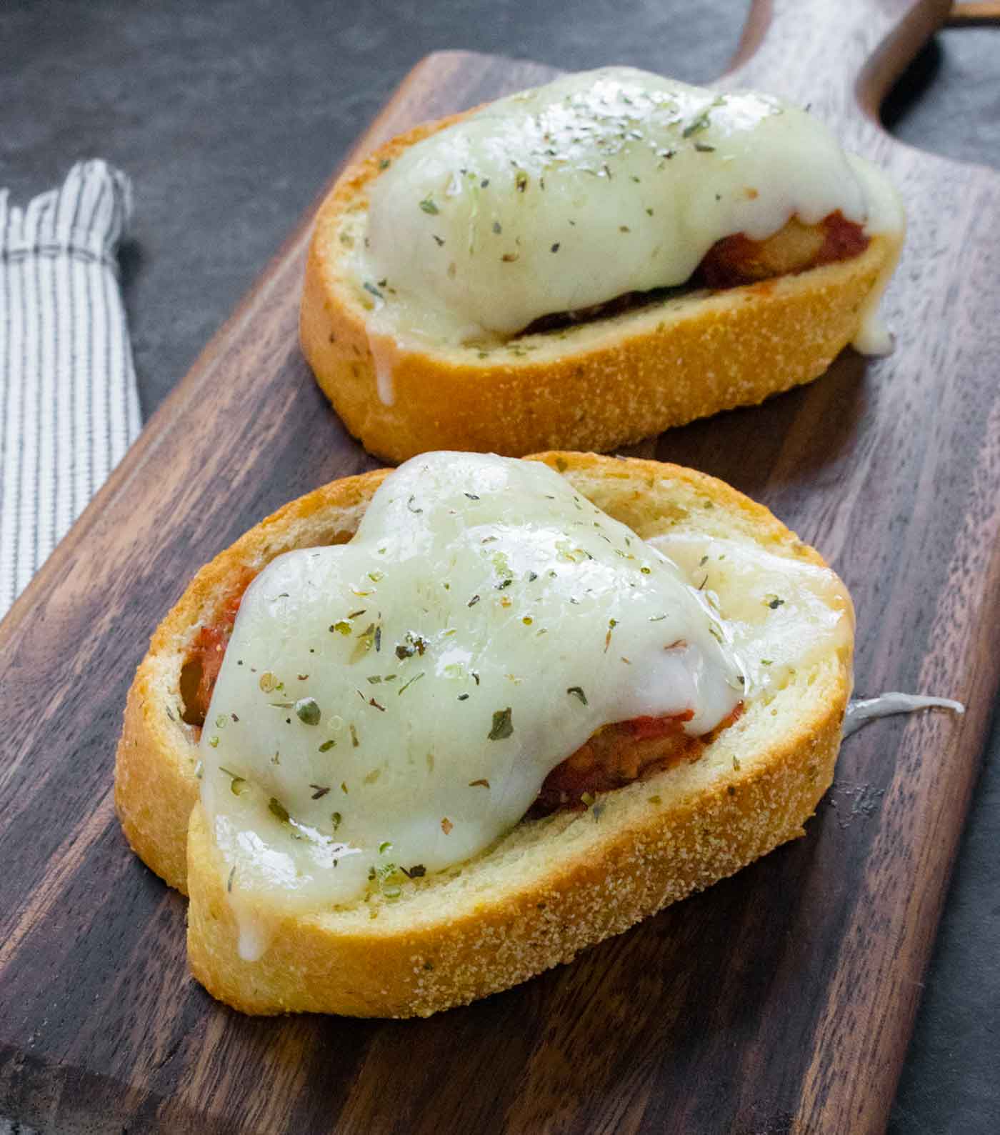 A side-angled view of two Meatballs on Texas Toast on a wooden serving board.