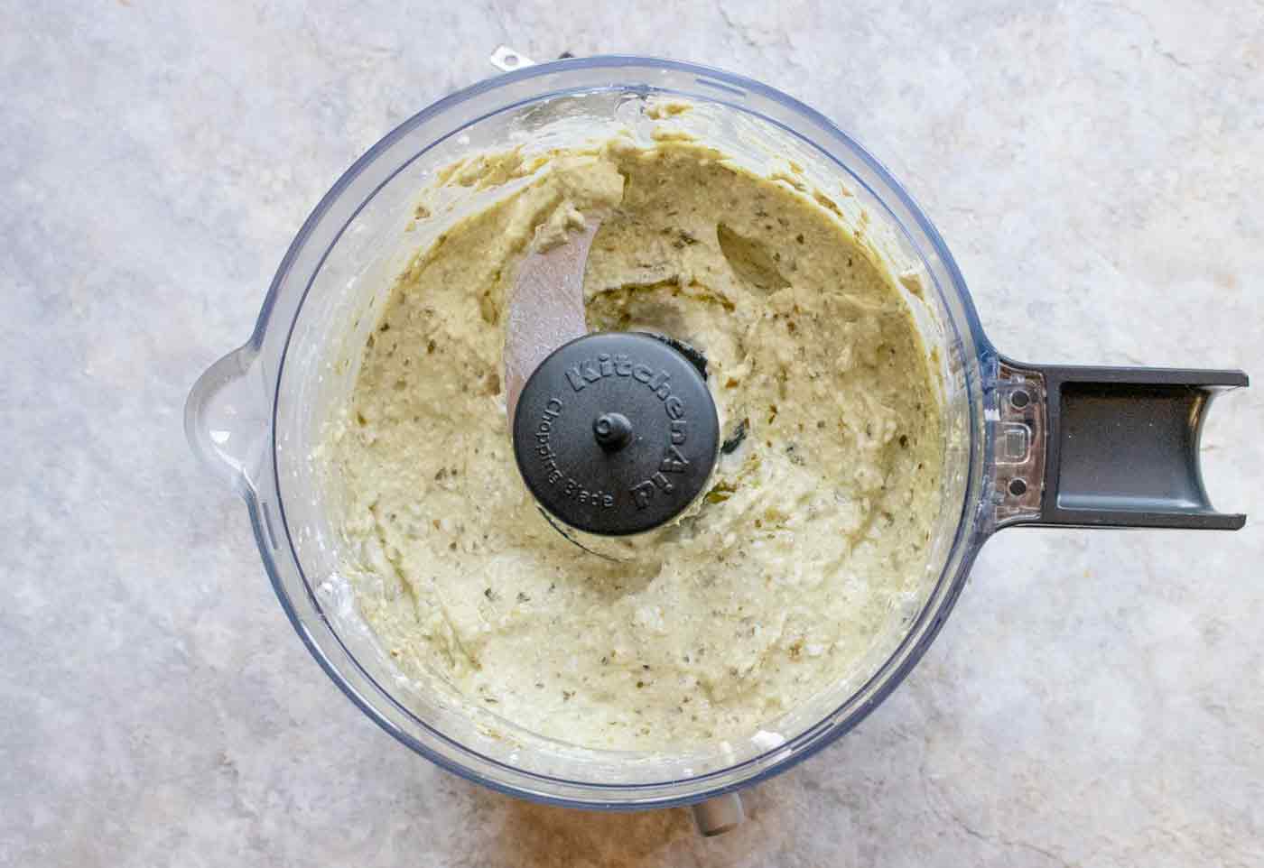 Overhead view of creamy pesto blended in a food chopper.