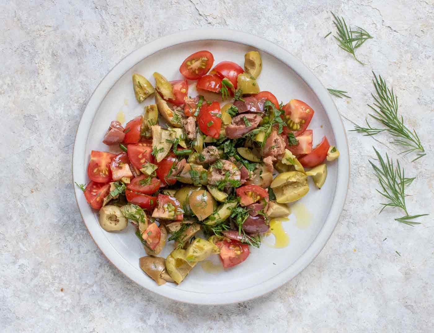 Overhead view of tomato and olive salad with herbs on a light gray plate.