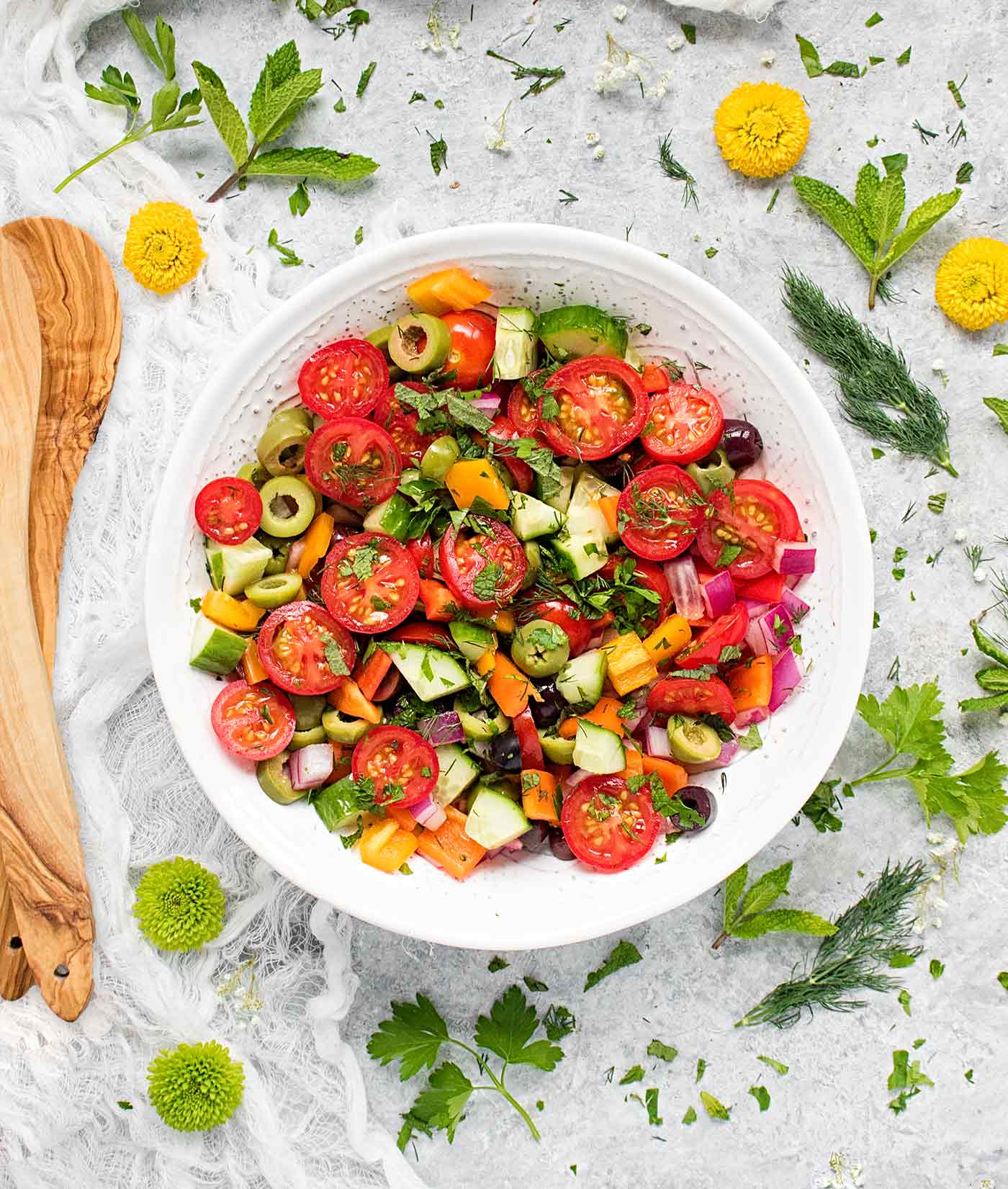 Mediterranean chopped salad in a large white bowl with wooden serving spoons