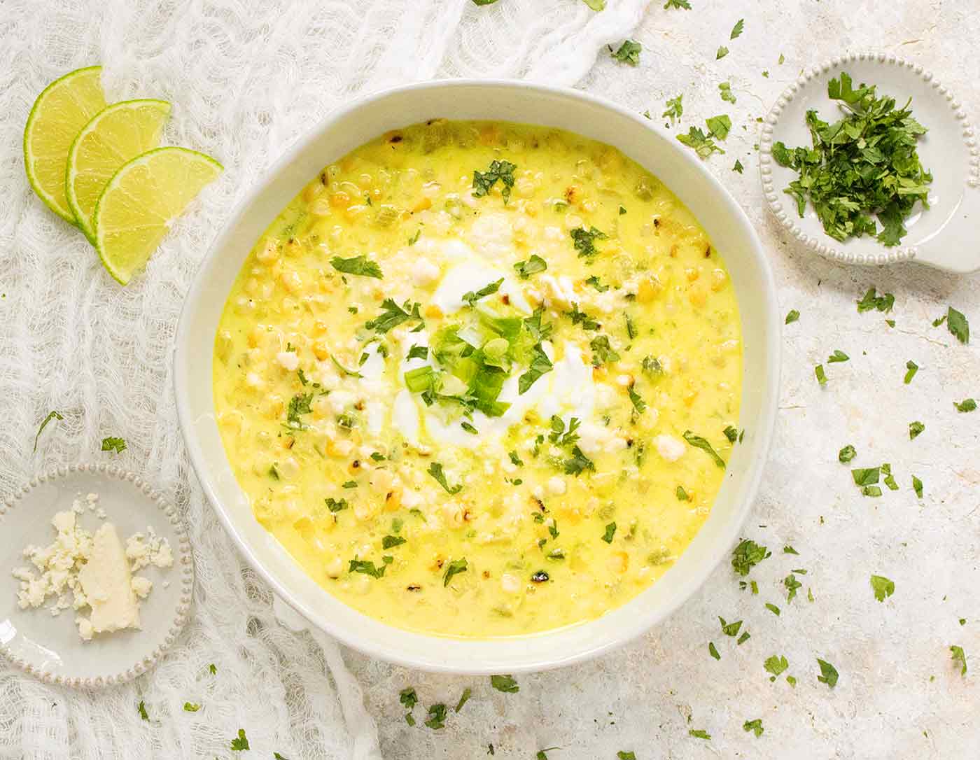 Mexican Street Corn Soup in a white bowl with cotija cheese and cilantro on the side
