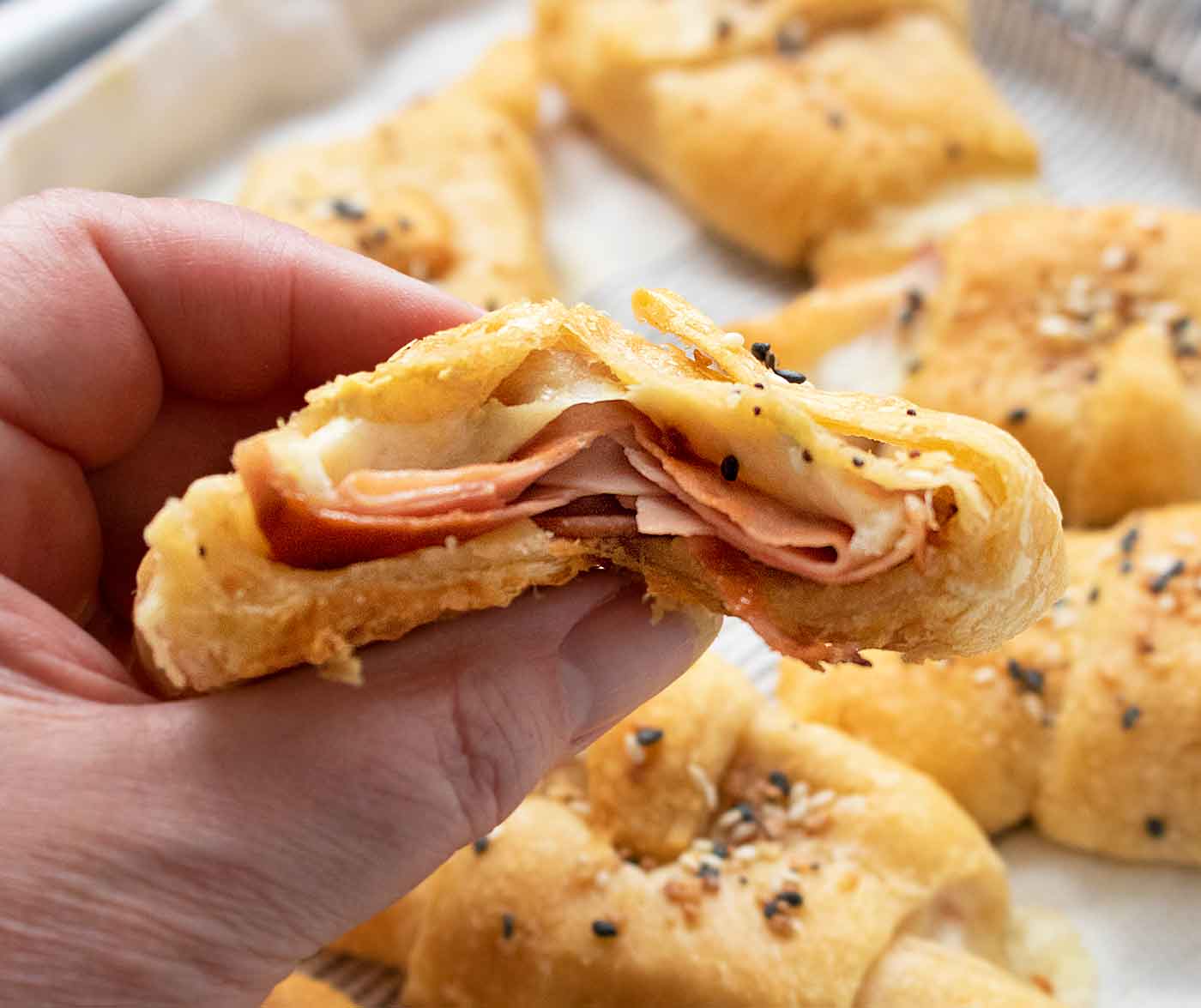 Hand holding a Mortadella Stuffed Crescent Rolls split in half so the meat and cheese inside are visible.