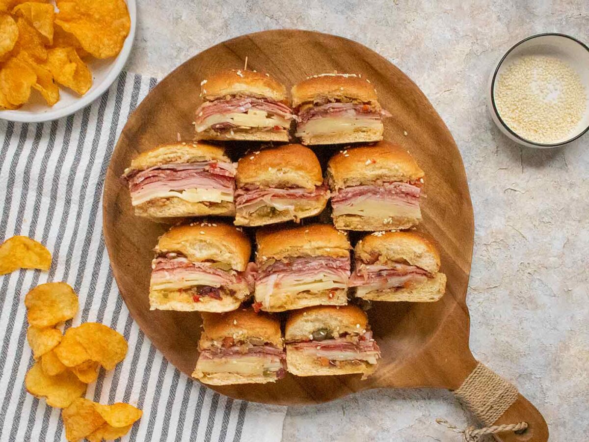 Muffuletta Sliders turned on their sides on a wooden serving tray.