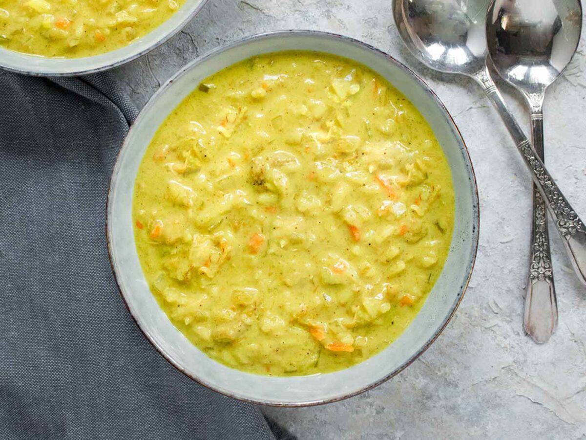 Mulligatawny Soup in a gray bowl with spoons on the side.