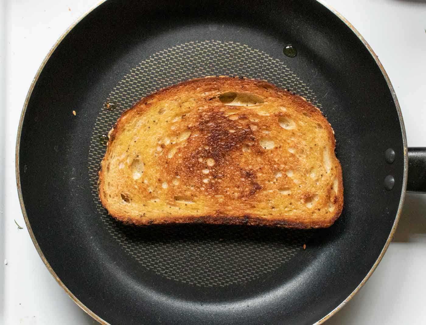 A slice of sourdough bread frying up in a skillet.